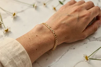 Bracelet femme La Vie en Or en chaîne fine dorée porté sur un poignet délicat posé sur du marbre blanc, vue macro élégante